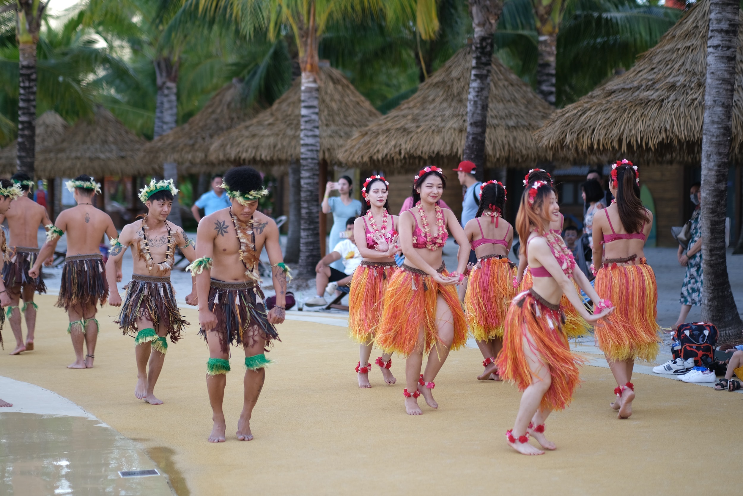 Dancers in grass skirts and palm crowns sway together on a beach, photo © T.H. Dao for pexels.com