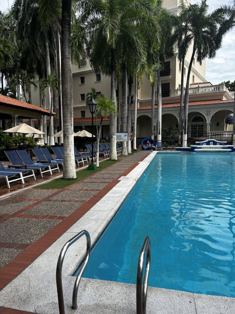 A glistening blue pool with chaise lounge chairs lined around its edge at Hotel el Prado in Barranquilla, Colombia, photo ©Kate Dana