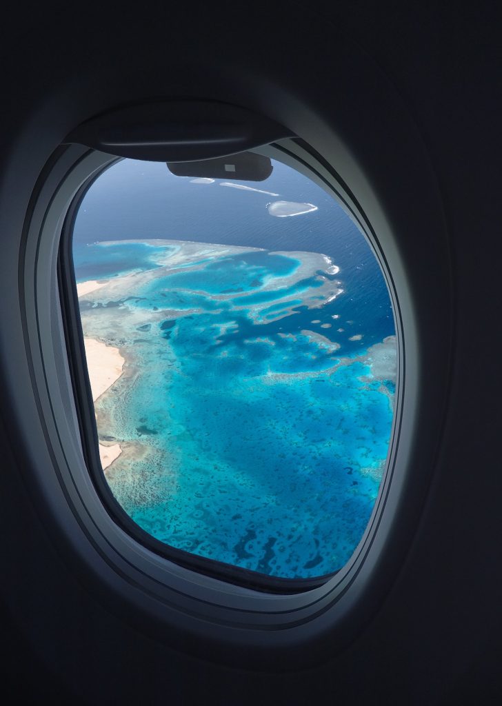 The window of an airplane showing an ocean with coral reefs, photo © Igor Fedoriv for Pexels