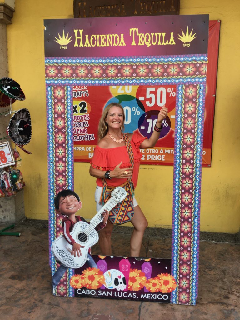 A person smiling stands inside a large, colorful frame near Centro in Cabo San Lucas, Mexico, photo ©Kate Dana