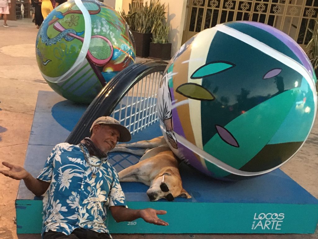 A man gestures playfully at a sleeping dog wearing sunglasses in the Marina of Cabo San Lucas, Mexico, photo © Kate Dana