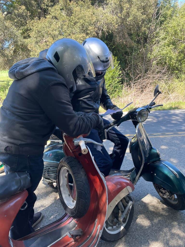 Two riders wearing helmets and riding gear on vintage Vespas, Italian motor scooters, stop to check the route map with their bikes along the daytime ride route for the annual Rides of March scooter rally in San Luis Obispo, CA, photo ©Kate Dana