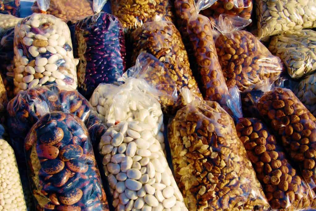 Bags of dried beans line a shelf in a store, among them shiny, small, red Pinquito beans known for their goodness when cooked, releasing their smoky, saucy flavor, a must-have meal in the Santa Maria Valley. Photo © bjgaowei2008 for pixabay