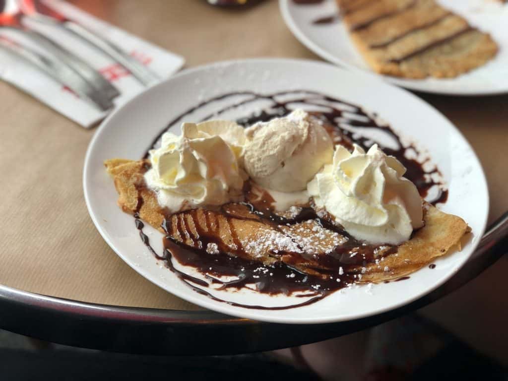 Banana and Nutella crepes with whipped cream and powdered sugar deliver sweetness and light on a white plate in this photo by Austin P for Unsplash.
