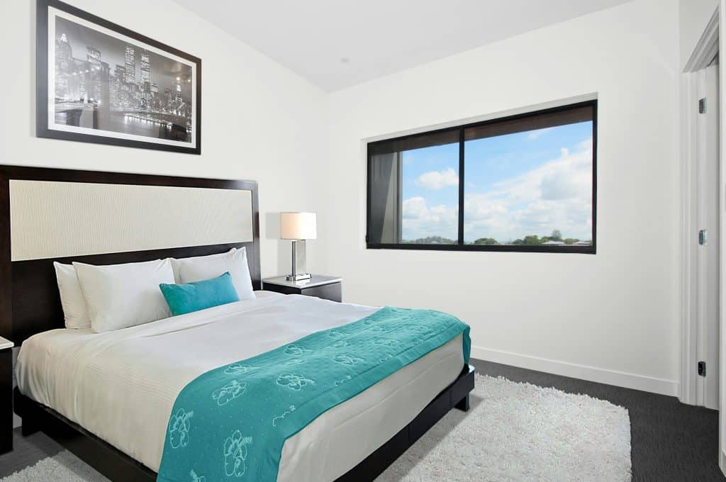 The interior of a hotel room, with a king-sized bed in white and blue sheets next to a window with a clear sky, similar to those in Santa Cruz, California, welcomes visitors for events like Morning Wood Classic Scooter Weekend, photo © Steven Ungermann for unsplash