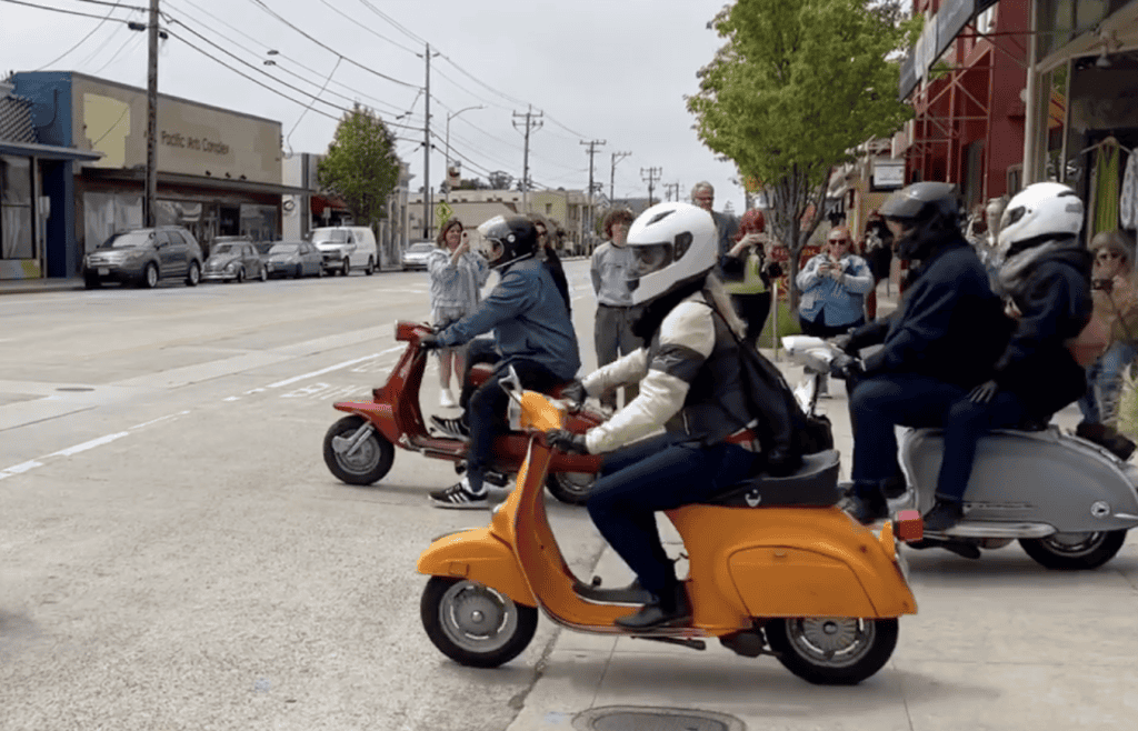 Scooterists ride out from a parking lot on a small frame vintage Vespa and a burgundy Lambretta in the morning at the start of Morning Wood Classic Scooter Weekend in Santa Cruz, California, photo ©Kate Dana