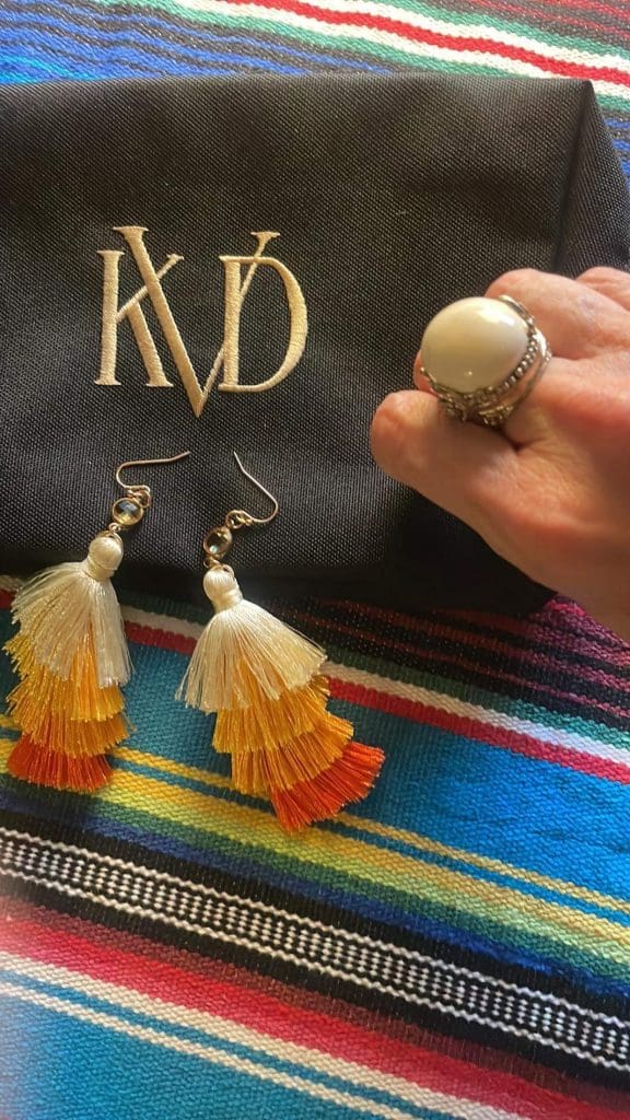 Beautiful, tri-color, tassel earrings lay on a small, black makeup bag by Kat Von D, featuring her initials, K-V-D, and a large, white bulbous cocktail ring are just many of the treasures found while thrift shopping in San Luis Obispo, near the Santa Maria Valley, California, photo © Kate Dana