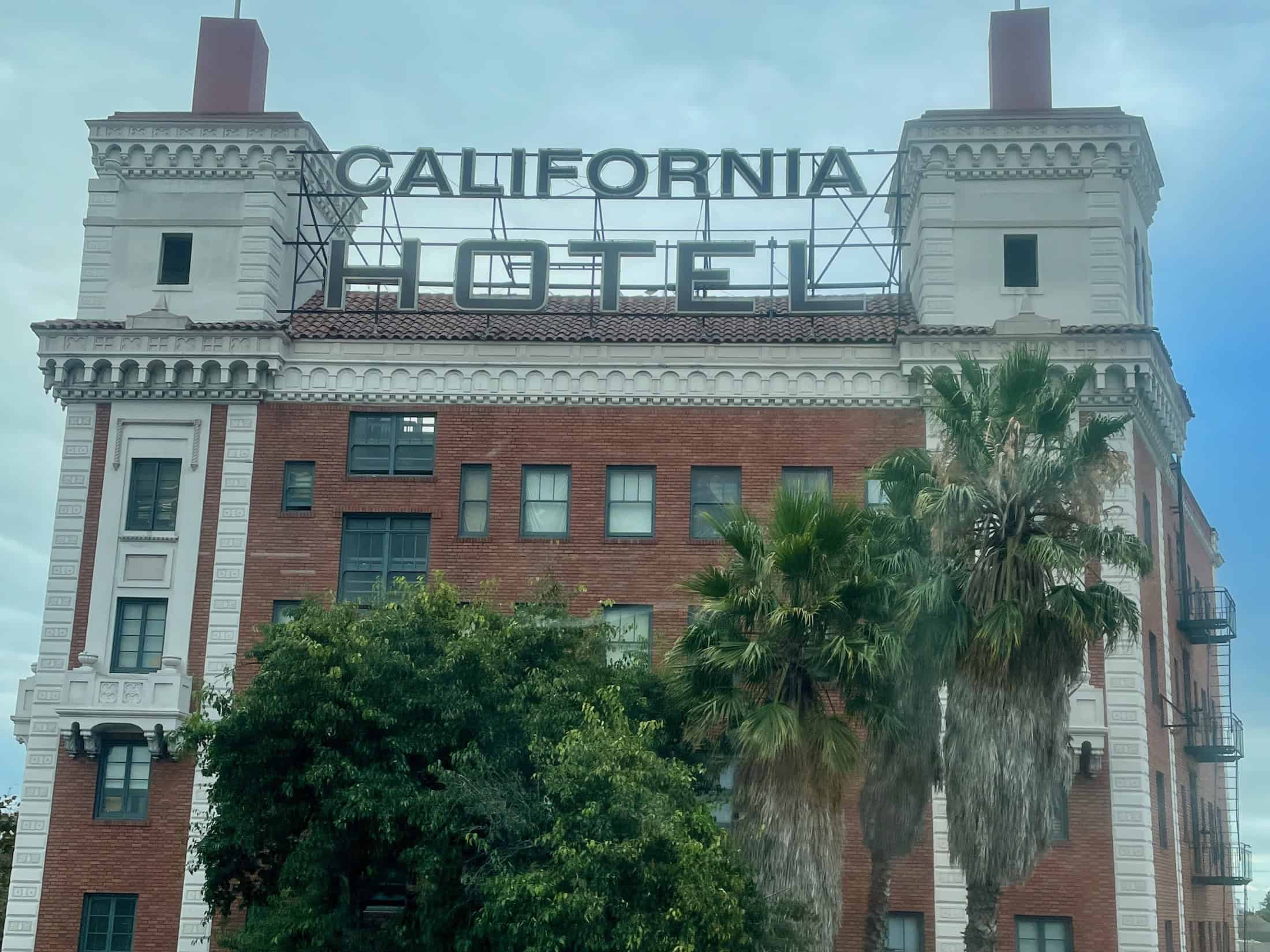 A highway view of the facade of the California Hotel, with its trees out front and sign across the top, features this iconic building in Oakland in this photo for 45 California Sayings to Get Stoked About Right Now, photo © Kate Dana