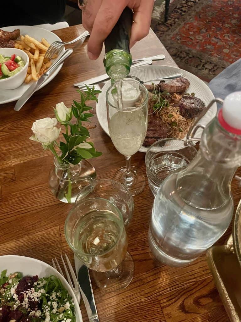 Authentic Levantine Cuisine is presented on white dishes on a table with non-alcoholic champagne being poured into a glass at Ammatoli in Long Beach, CA, home of Long Beach Classic Scooter Club's annual Classic Not Plastic Scooter Rally on Memorial Day weekend, photo ©Kate Dana