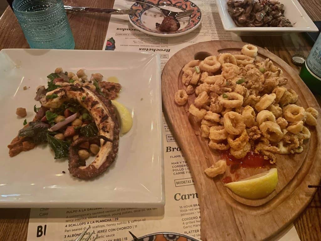 Delicious, grilled calamari steak served on a white ceramic dish next to a large plate of golden, fried calamari on a wooden board adorn the table at food establishment Café Sevilla in Long Beach, CA, home of Long Beach Classic Scooter Club's annual Classic Not Plastic Scooter Rally on Memorial Day weekend, photo ©Kate Dana