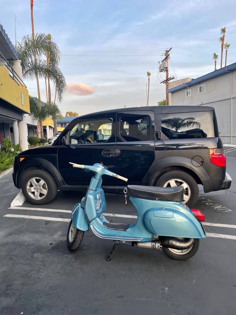 A small, blue, vintage Vespa sits beside a black Honda Element in the parking lot outside of a room at Hotel Current in Long Beach, CA, for Long Beach Classic Scooter Club's annual Classic Not Plastic Scooter Rally on Memorial Day weekend, photo ©Kate Dana