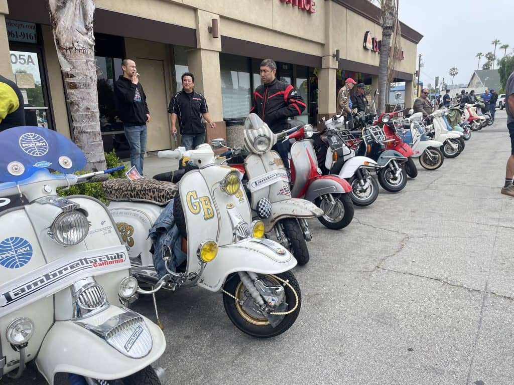 Dozens of vintage Vespas and Lambrettas, sit parked, lined up in front of DiPiazza's pizza place in  Long Beach, CA, home of Long Beach Classic Scooter Club's annual Classic Not Plastic Scooter Rally on Memorial Day weekend, photo ©Kate Dana