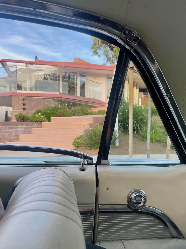 A midcentury modern home, with a pink facade, angled roof, and green landscaping, is viewed from the window of a 1963 Ford Thunderbird in this photo taken in Long Beach, CA, home of Long Beach Classic Scooter Club's annual Classic Not Plastic Scooter Rally on Memorial Day weekend, photo ©Kate Dana