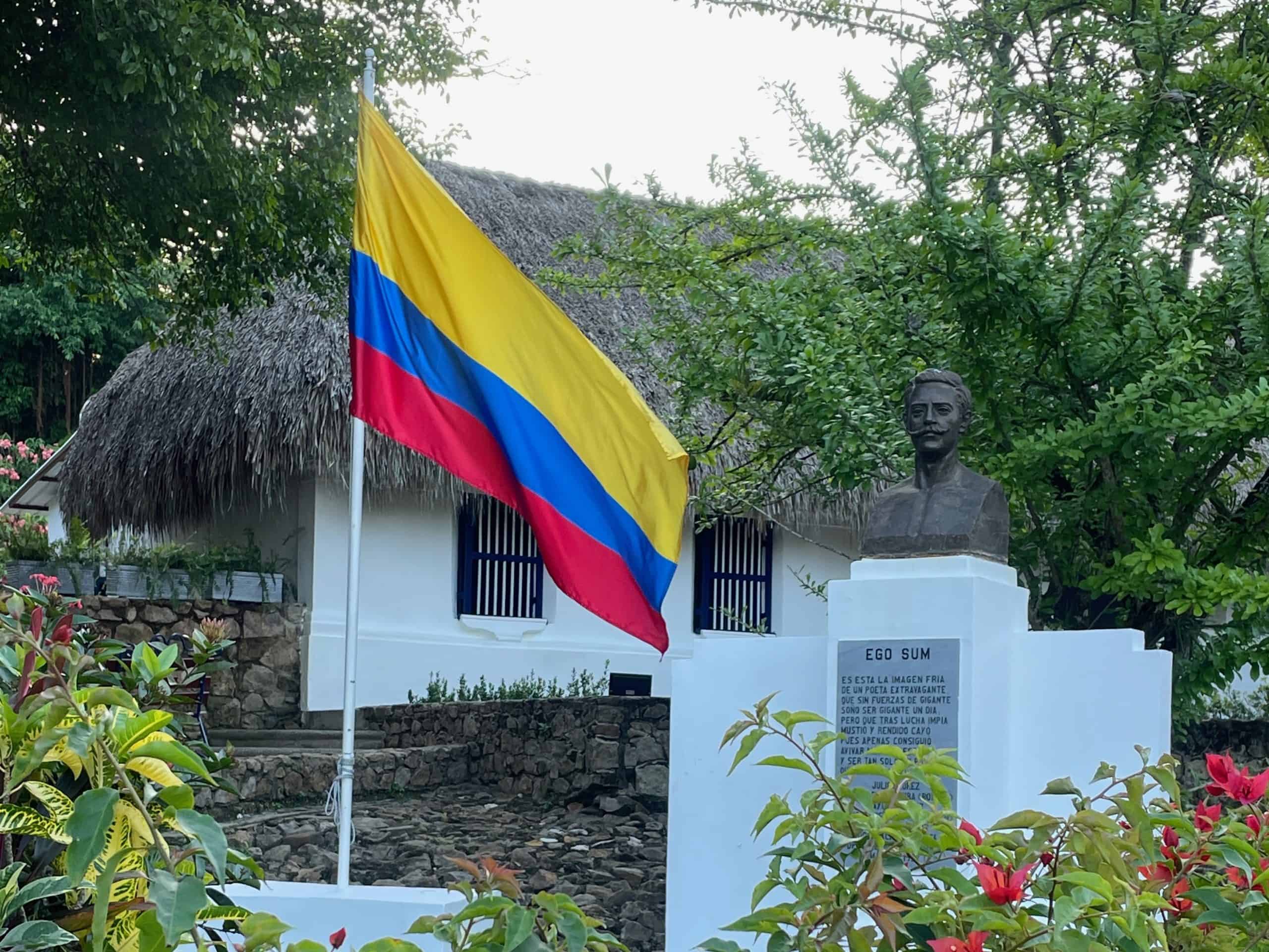 A yellow, blue, and red Colombian flag flies next to a sign for the Inmueble Patrimonial Poeta Julio Florez in Usiacuri, Colombia, photo ©Kate Dana