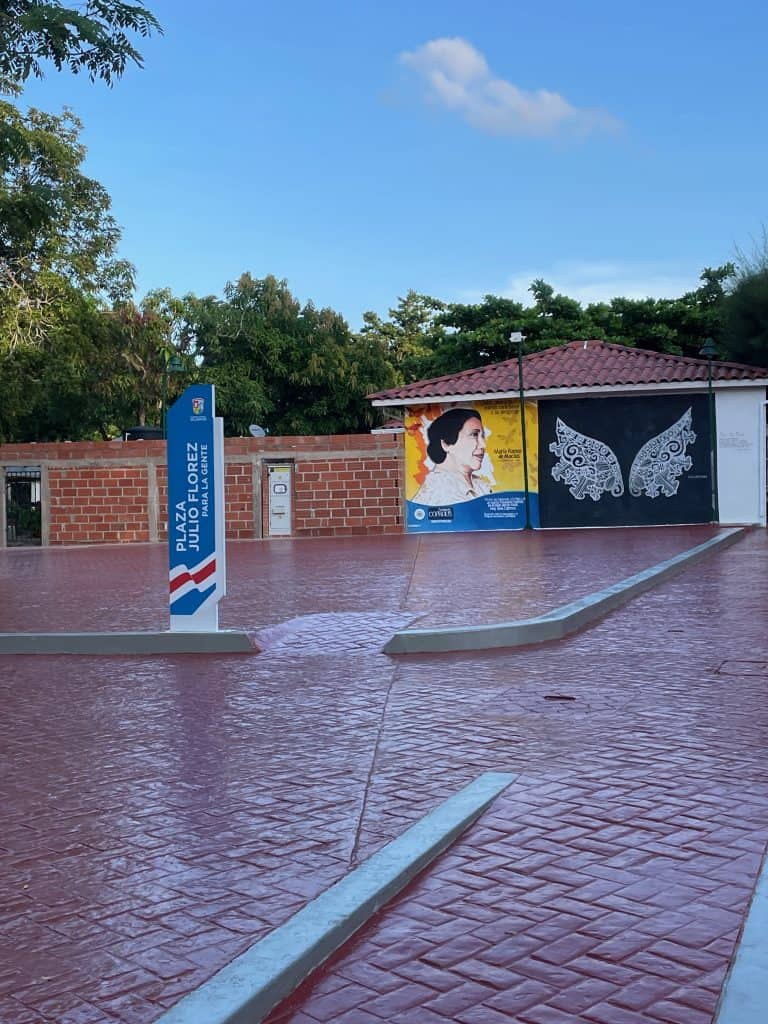 Shiny red bricks line the ground next to colorful murals in Plaza Julio Florez during a day in enchanting Usiacuri, Colombia, photo ©Kate Dana