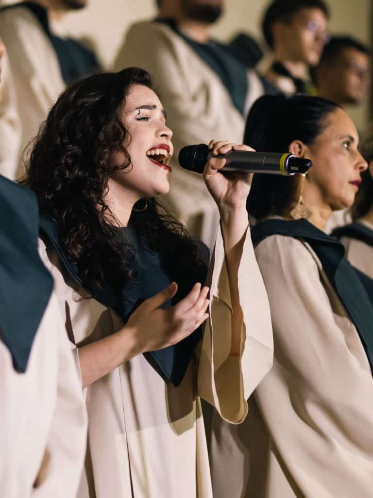 "You're preaching to the Choir": Several dark-haired singers in church robes sing into microphones inside a church in this color, close-up photo for 78 Southern Phrases to Blow Your Hair Back, Cocameca.com photo © Canva