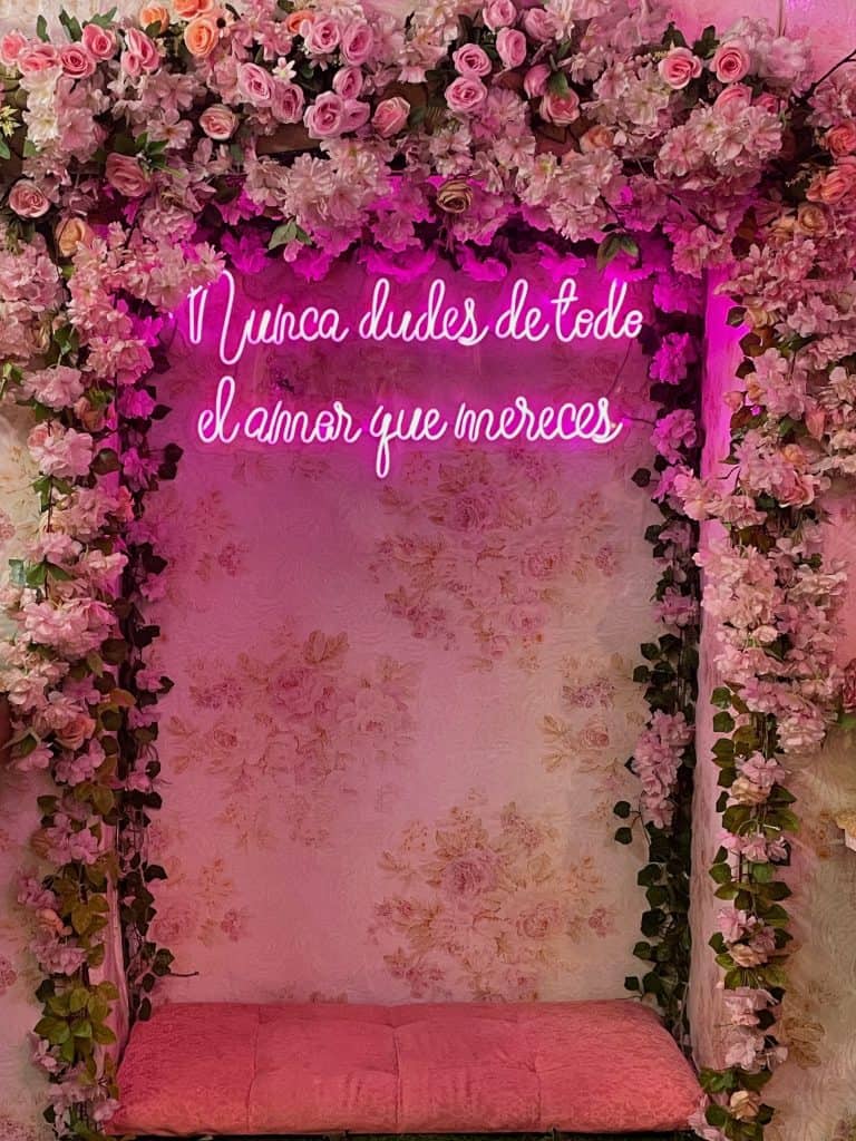 A bright pink neon sign reads "Nunca dudes de todo el amor que mereces" - Never doubt all the love you deserve- against pink roses and a pink wall in this photo from Cartagena, Colombia by ©Kate Dana
