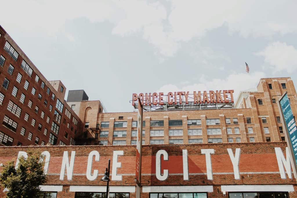 A large neon red sign high above a white-letter painted sign on a brick wall announce the location of Ponce City Market in Atlanta, GA, photo ©Emma Valerio for Unsplash