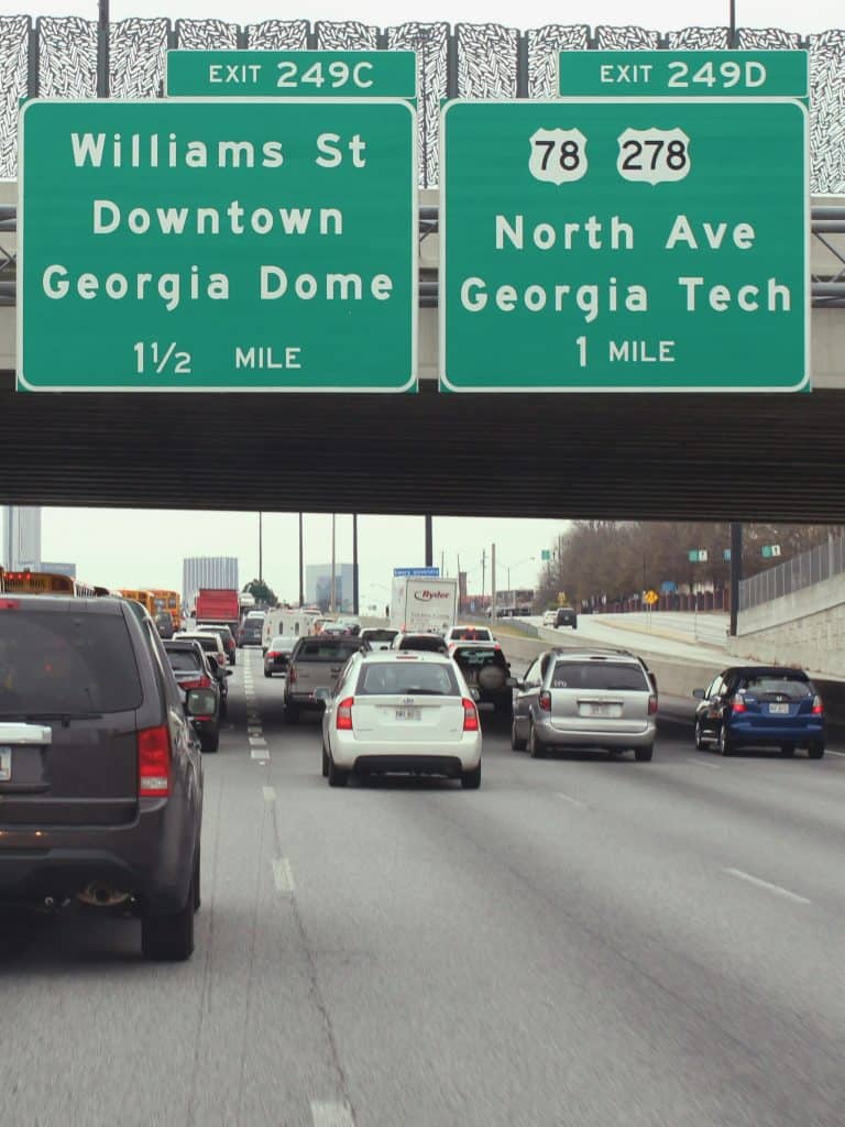 Cars on a busy expressway near Atlanta, GA pass under green and white signs announcing exits for downtown and Georgia Tech, a typical scene when you explore Atlanta like a local, photo ©Melvin Chavez for Unsplash