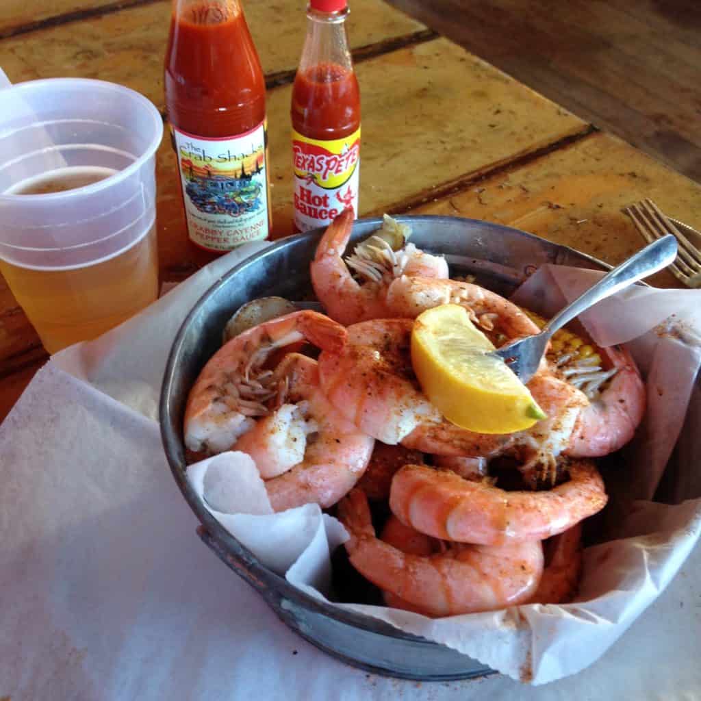 An aluminum bucket of fresh-cooked shrimp boiled with lemon and corn sits on a table next to bottles of hot sauce and a pint of beer at Rita’s on Folly Beach, near Charleston, S.C, a city similar to Cartagena, Colombia, photo ©Kate Dana