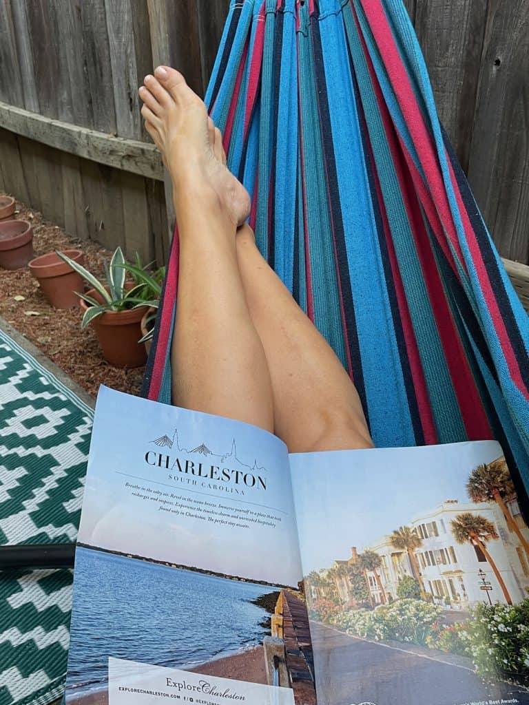 A person relaxes in a blue and red striped cotton hammock from Colombia, holding a glossy magazine against their bare legs, reading about Charleston, S.C, a city similar to Cartagena, Colombia, photo ©Kate Dana