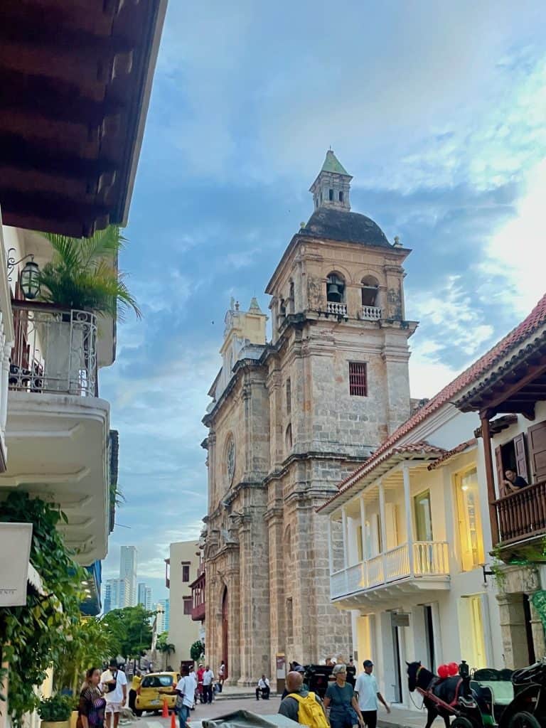 The strong towers of Catedrál San Pedro Claver rise over a city street on a sunny afternoon in the Centro in Cartagena, Colombia, a city similar to Charleston, S.C., photo ©Kate Dana