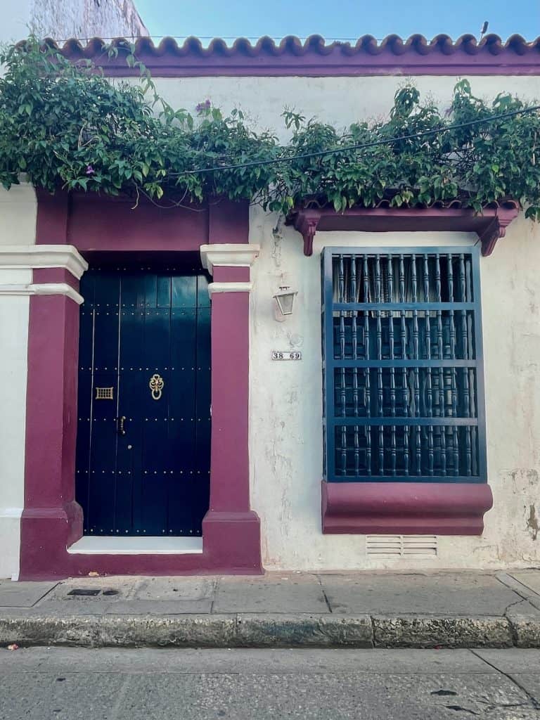 A bold purple and cream colonial building with a large wooden door and greenery near the roof graces the streets of the Centro in Cartagena, Colombia, a city similar to Charleston, S.C., photo ©Kate Dana