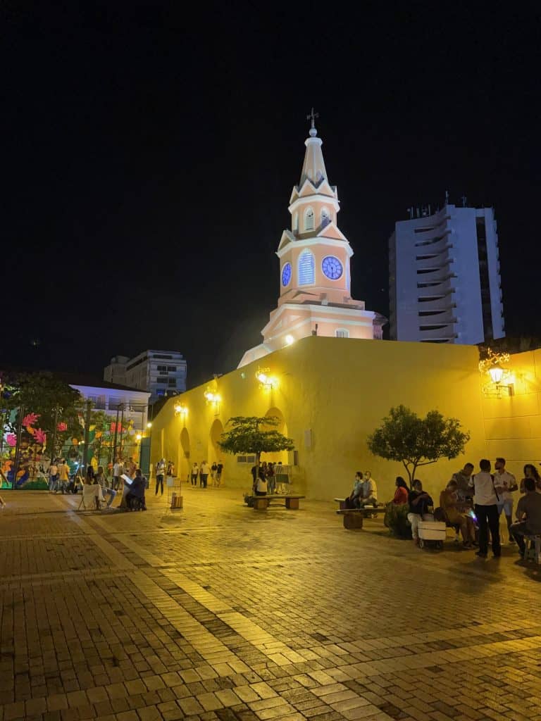 The gold and white Torre de Reloj, Clock Tower, glows against a night sky at the entrance to the Plaza de los Coches in Cartagena Colombia, a city similar to Charleston, S.C., photo ©Kate Dana