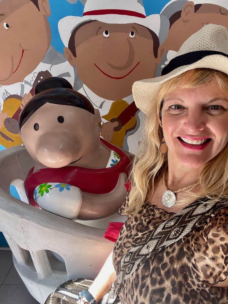 Cocameca founder Kate Dana smiles in the colorful interior with souvenirs and ceramic characters at La Casa de Donia Way Tienda de Artesanos in Merida, Mexico, photo ©Kate Dana