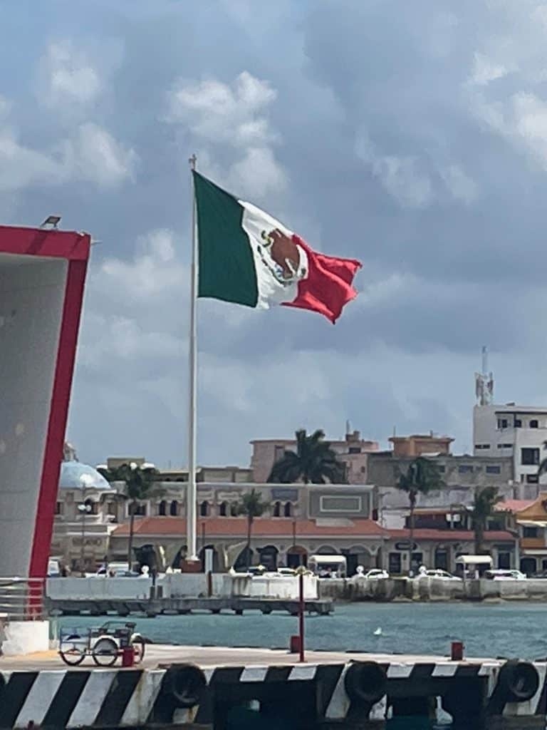 A huge green, white, and red Mexico flag flies over the harbor on a sunny day on Isla Cozumel, Quintana Roo, adding to the article Mexican Slang for Beginners: Phrases to Know photo ©Kate Dana