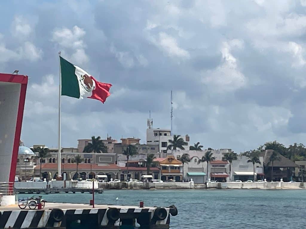 A huge green, white, and red Mexico flag flies over the harbor on a sunny day on Isla Cozumel, Quintana Roo, adding to the article Mexican Slang for Beginners: Phrases to Know photo ©Kate Dana