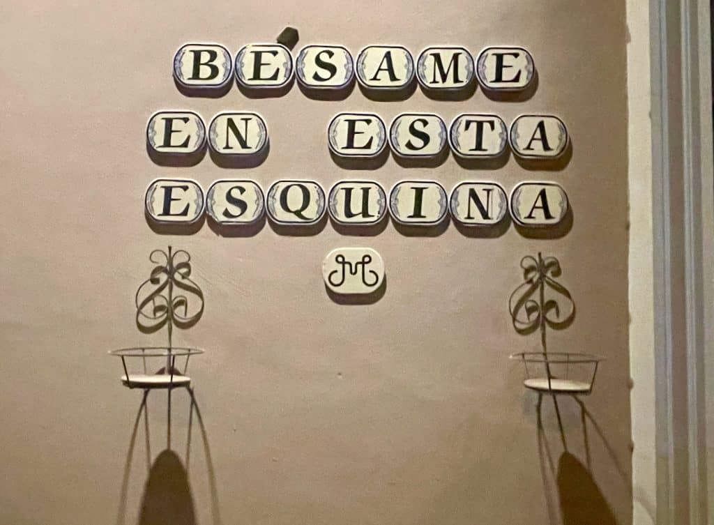 Blue text on cream colored tiles make up the phrase, "Besame en esta esquina" translates to "kiss me at this corner," mounted to a wall in Merida, add to the article Mexican Slang for Beginners: Phrases to Know photo ©Kate Dana