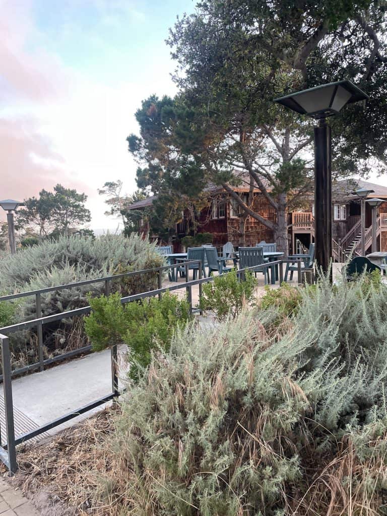 A rustic, wood boardwalk winds beside large houses with flat patios and welcoming chairs near the beach at Asilomar Hotel & Conference Grounds, located on the Monterey Peninsula in Pacific Grove, CA photo ©Kate Dana