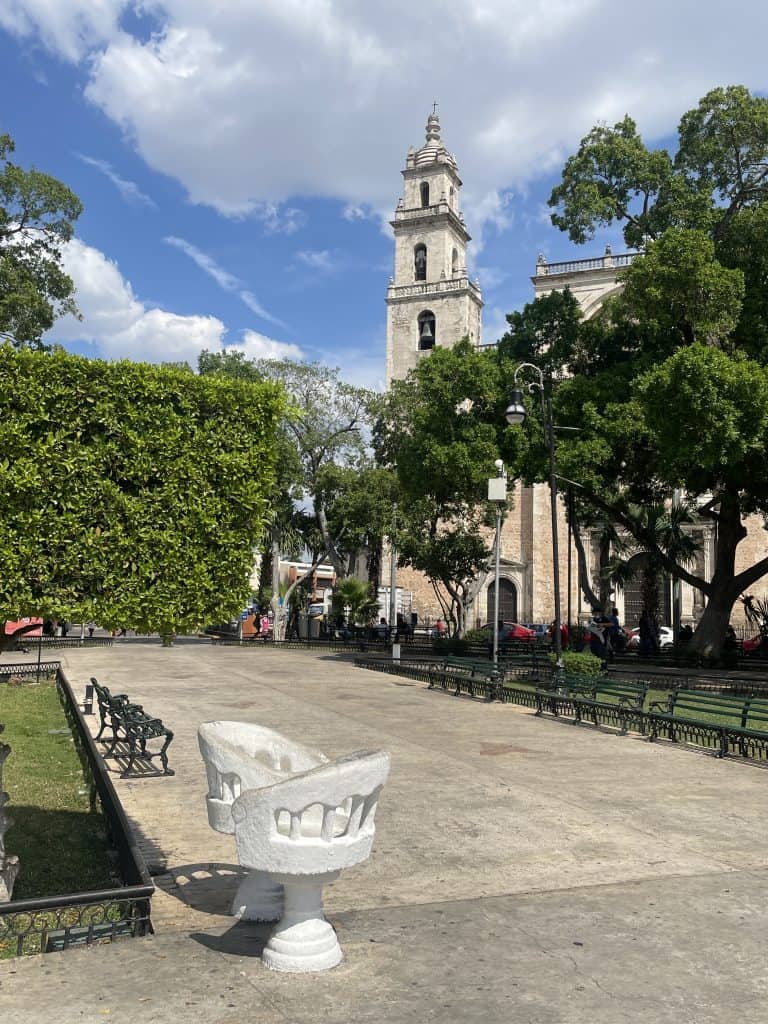 A conversation silla - a curved chair for two people found in Merida, Mexico, in the main plaza with a cream-colored church tower in the background, photo ©Kate Dana