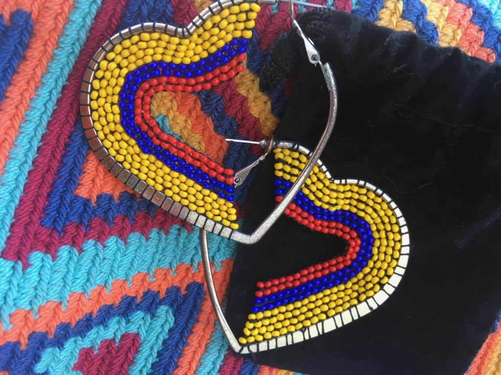 Heart-shaped, handmade beaded earrings in yellow, blue, and red rest on a colorful handwoven mochila from Colombia, photo ©Kate Dana