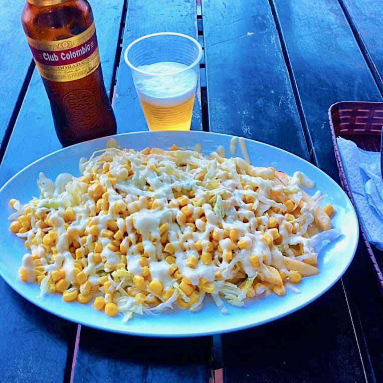 A plate of desgranada, corn with creamy salsas, and a chilled bottle of Club Colombia beer on a table, photo ©Kate Dana