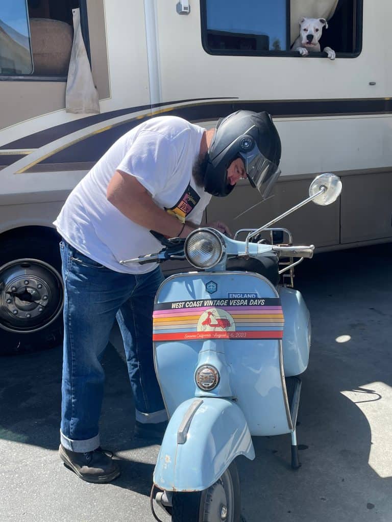 Gareth Richards, one of the organizers of West Coast Vintage Vespa Days 2024 in Santa Barbara, checks his blue vintage scooter in Santa Rosa, CA, photo ©Kate Dana