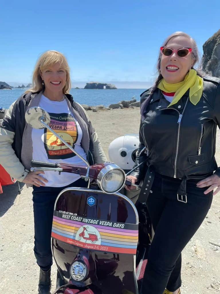 Two scooter riders with their vintage bikes pose in front of the ocean near Los Gatos, CA during West Coast Vintage Vespa Days 2023, photo ©Kate Dana