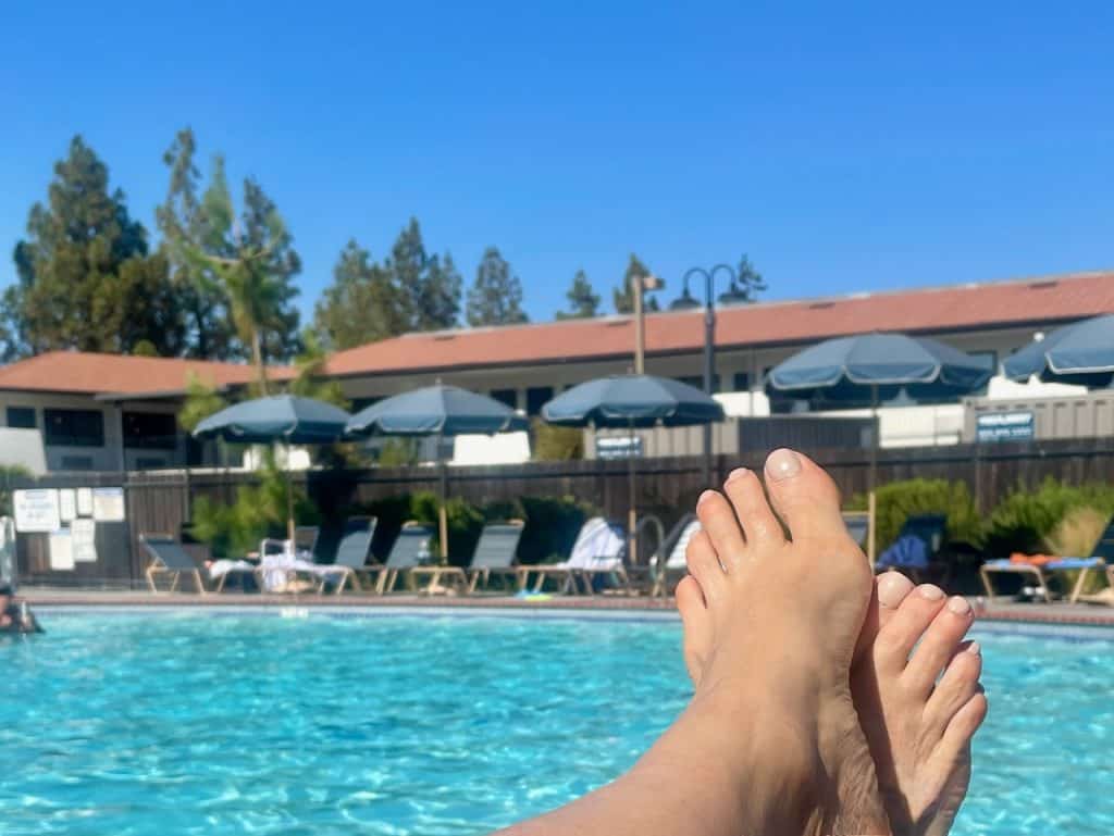 A close-up of toes with a shimmering blue pool and tables in the background at The Sandman hotel in Santa Rosa, CA, photo ©Kate Dana