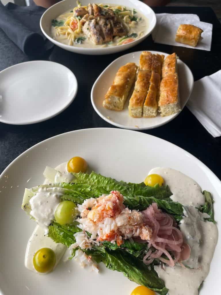 Ceviche with a cream sauce and breadsticks on plates sit on a table facing a plate of pasta Alfredo, photo ©Kate Dana