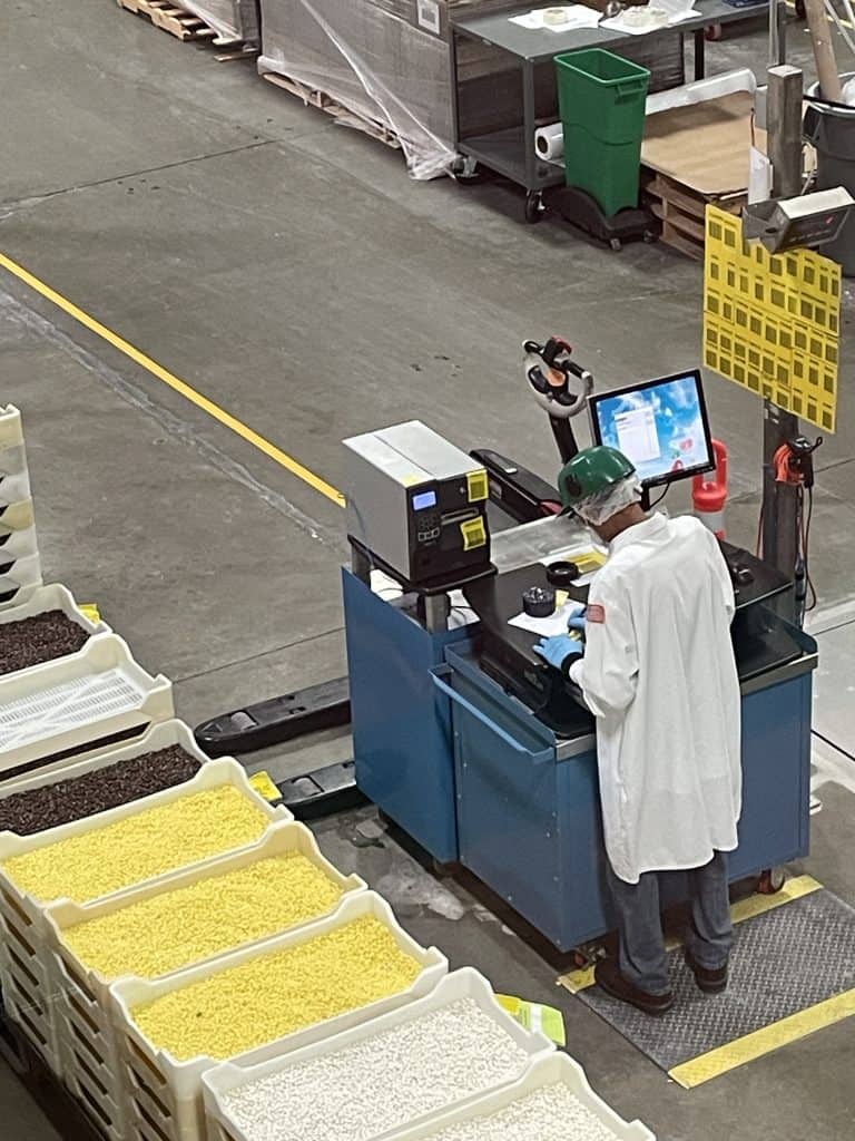 A worker dressed in a white lab coat, wearing protective eye goggles, take precise measurements at a calculation machine inside the Jelly Belly Factory in Fairfield, CA, photo ©Kate Dana