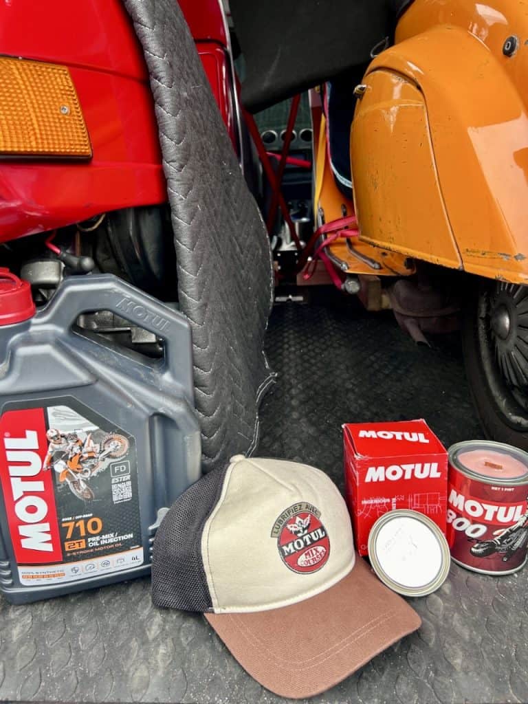 Raffle prize items from Motul on the floor of a van, including a half-gallon of oil, a sports cap, and a candle, photo ©Kate Dana