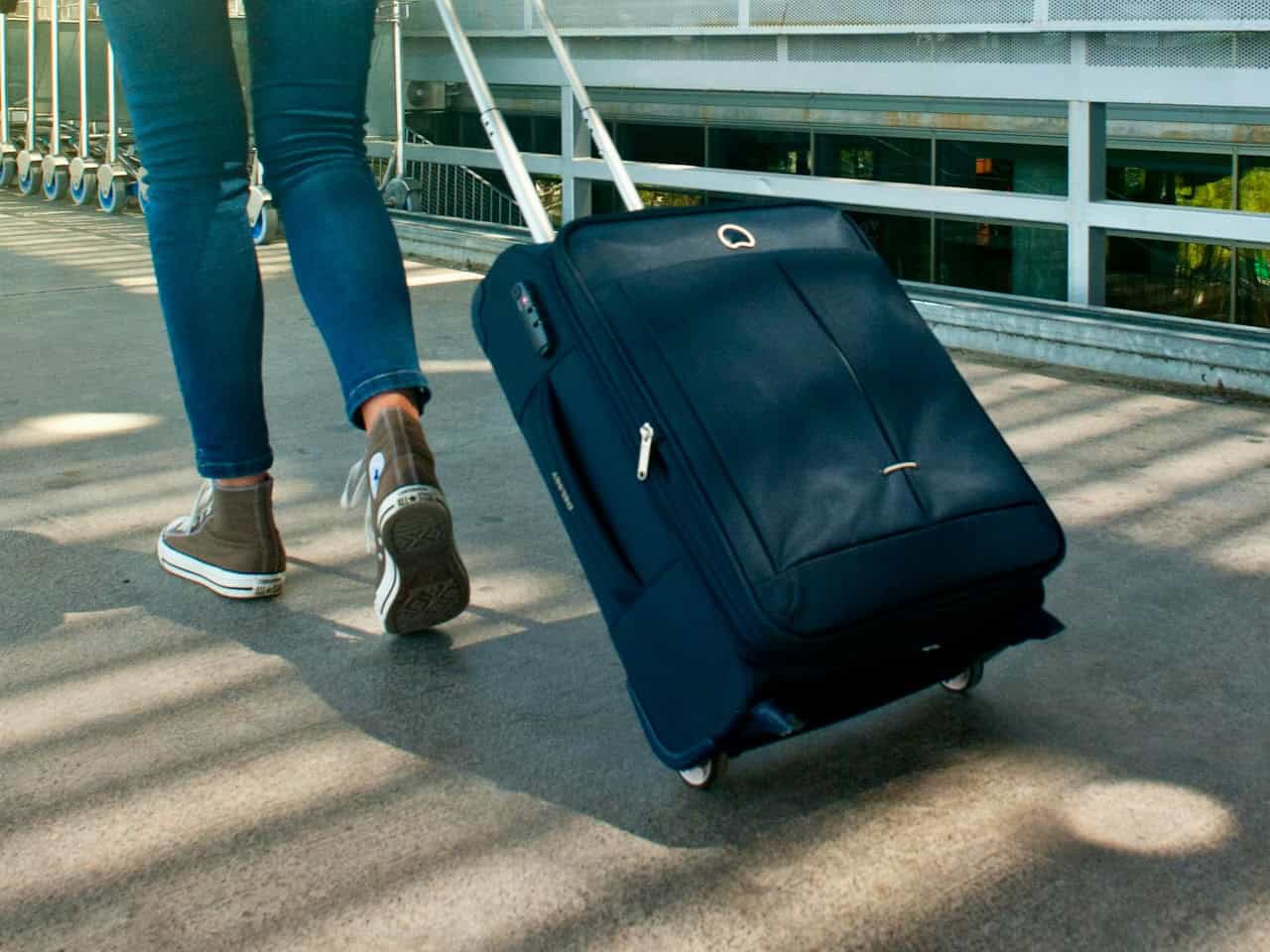 A person wearing jeans and athletic shoes pulls a black carryon suitcase, photo ©Freestockpro for Pexels