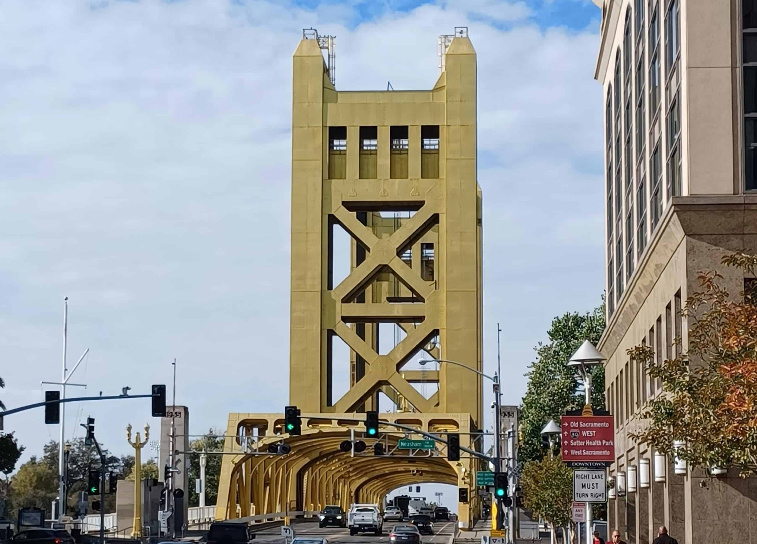 A street view looking over the river at the gold-painted Tower Bridge in Sacramento, CA, photo © Alex Ohan for Pexels
