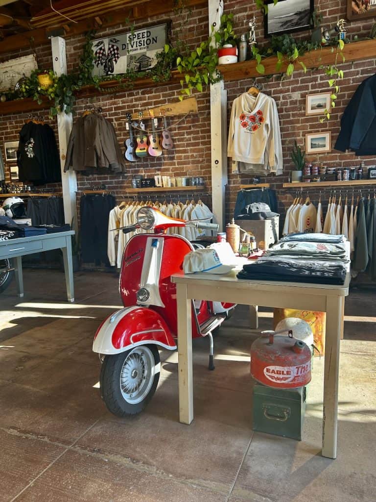 A table with merchandise next to a vintage Vespa scooter inside Esteem Surf Co, Pismo Beach, CA