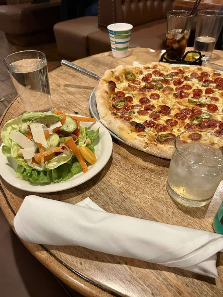 A pepperoni and hot honey pizza next to a salad on a table at Giuseppe's Italian American Club in Pismo Beach, California