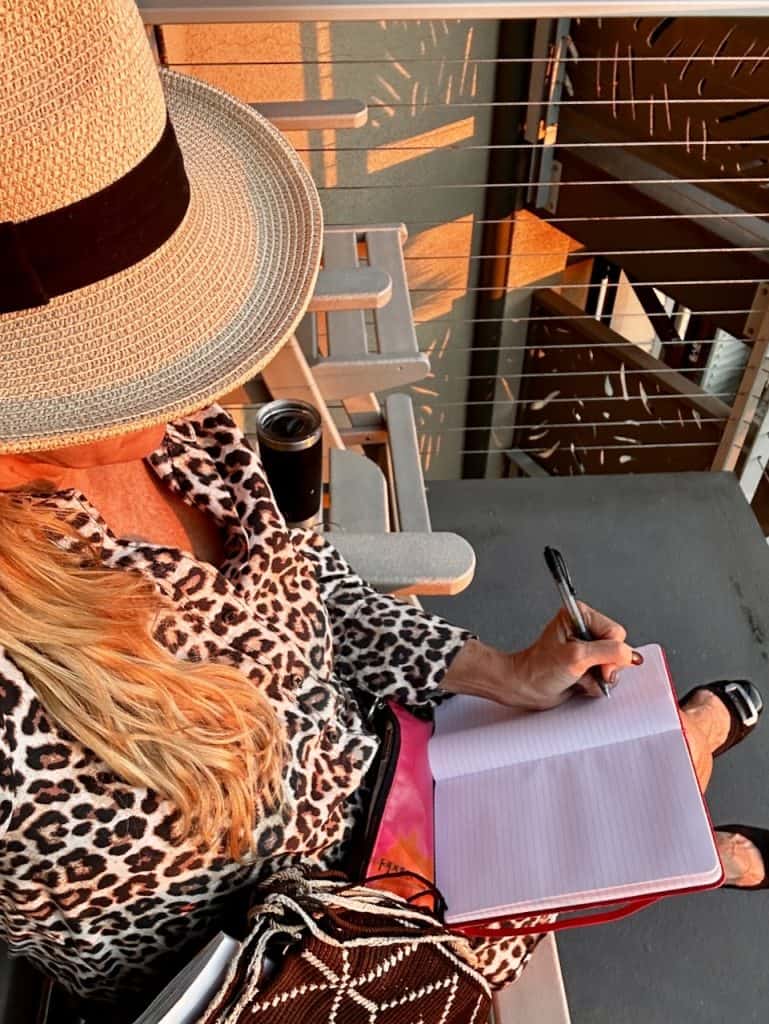 A traveler in a hat writes in a journal during Golden Hour at Inn at the Cove near Pismo Beach, California