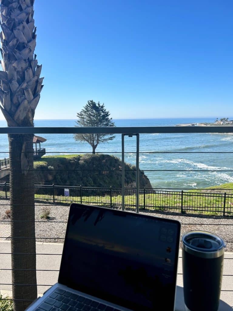 An open laptop faces out to a beautiful ocean view from a balcony at Inn at the Cove near Pismo Beach, CA