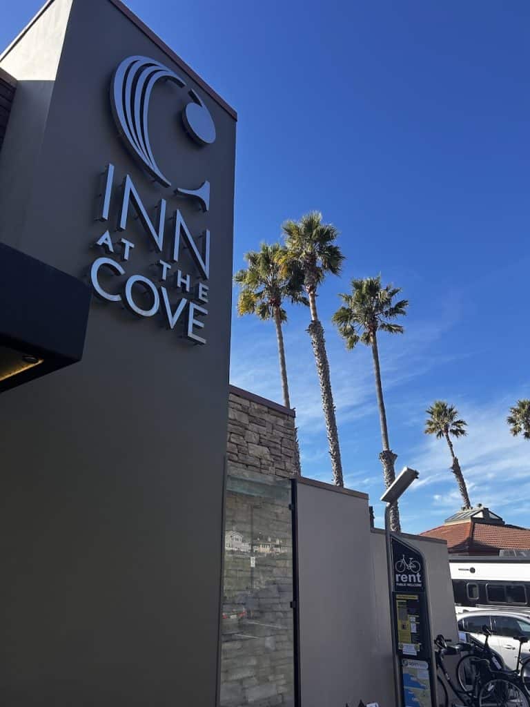 A sign announcing Inn at the Cove in Pismo Beach with palm trees against a blue sky