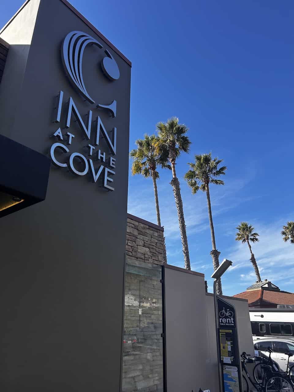 A sign announcing Inn at the Cove in Pismo Beach with palm trees against a blue sky